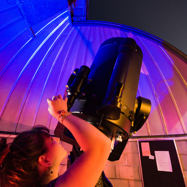 A student angles a telescope through an opening in an observatory roof