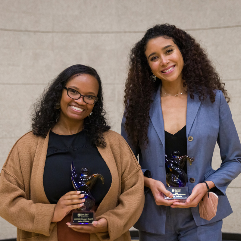 Two women smile while holding blue glass award statues