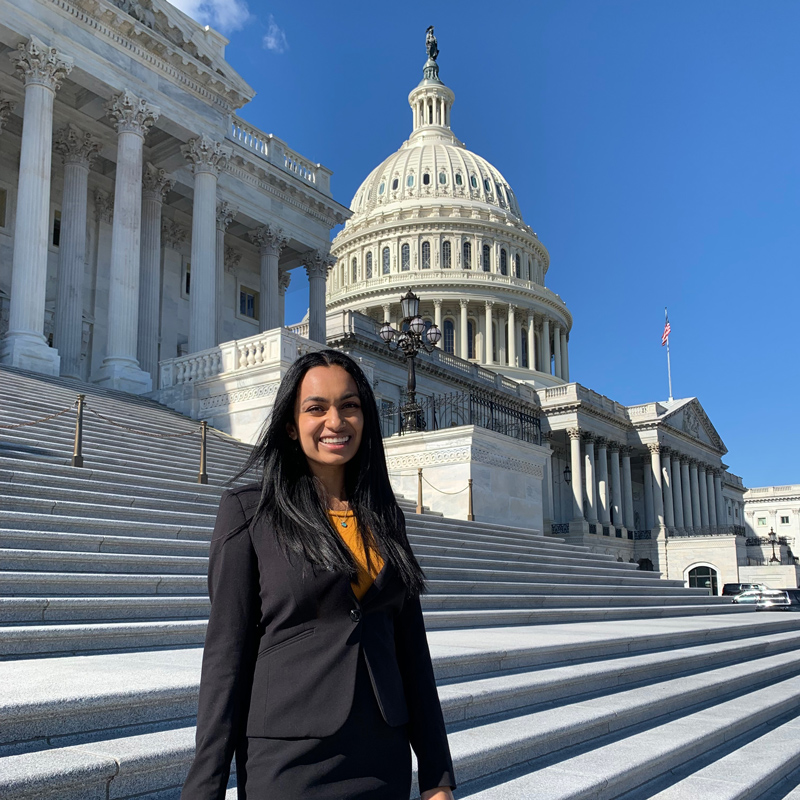 A person in a black blazer smiles while standing on the Capitol Building steps in Washington, D.C.