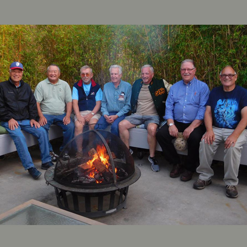 Seven people smile while sitting around a fire pit
