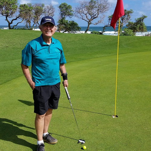 Grant Calkins holds a putter on the green near a red flag and the ocean