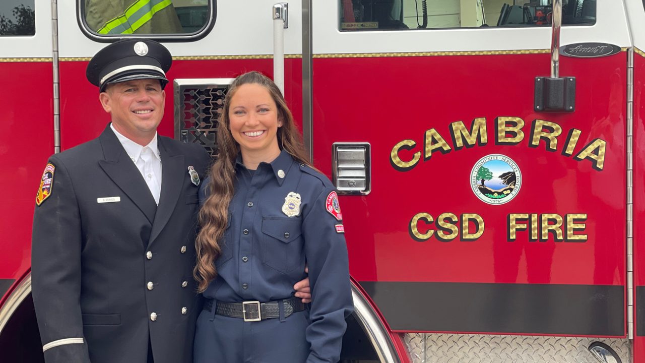 Kayla Graves stands in uniform in front of a red fire truck with another fire department employee