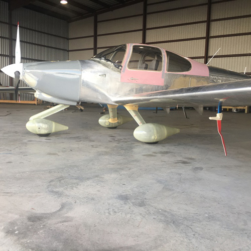 A small private aircraft with red primer sits in a hangar