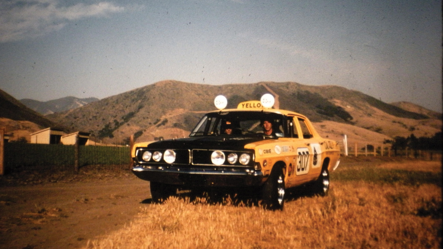 The original baja taxi drives down a dirt road with mountains in the background