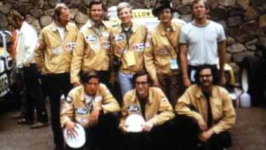 Eight members of the Baja Taxi team wear gold jackets in front of the car at the start of the race in 1972