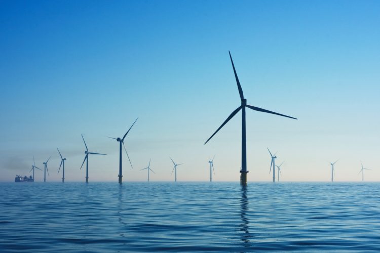 A series of wind turbines float on the surface of the ocean in front of a blue sky