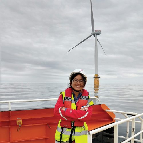 Researcher Yi-Hui Wang wears a helmet, life jacket and reflective vest in front of an offshore wind turbine near Scotland