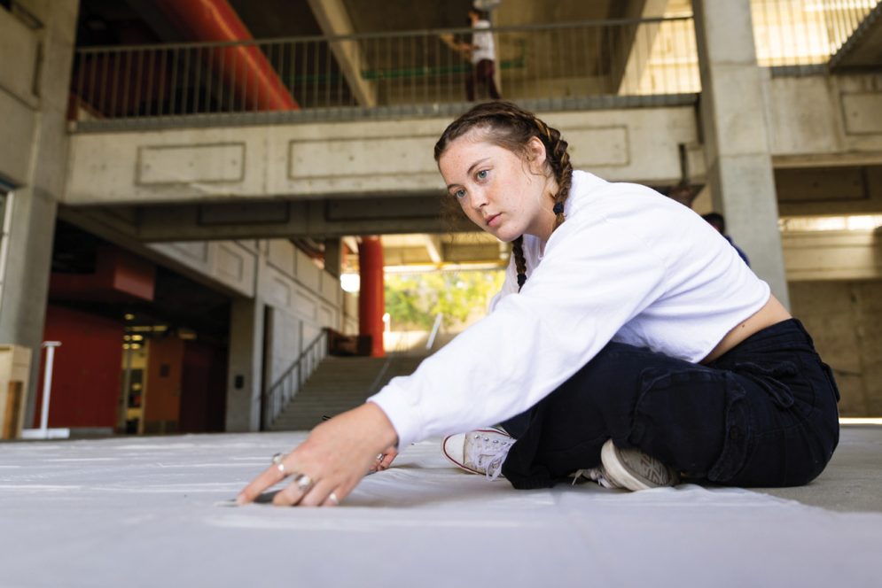 A student wearing a white sweatshirt sits while measuring yards of white canvas