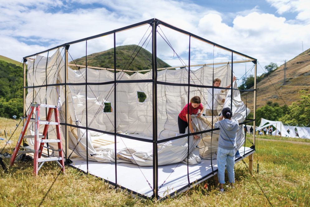 Three students construct a large square structure using canvas in Poly Canyon