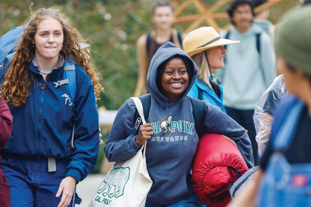 Two students carry camping gear, bags and sleeping bags