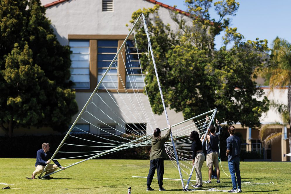 A students assembles a triangular structure using aluminum, steel and rope on Dexter Lawn