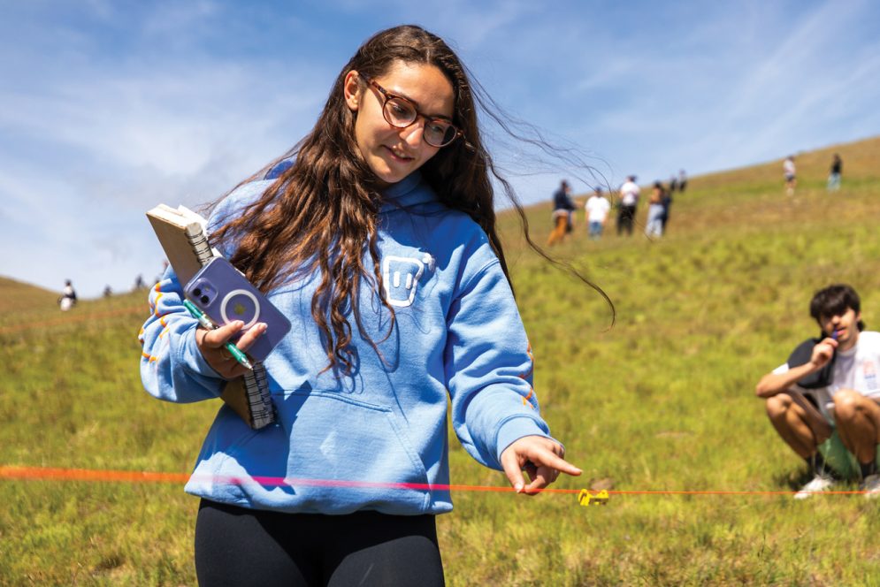A student in a blue sweatshirt points to a line level in the grass at Poly Canyon