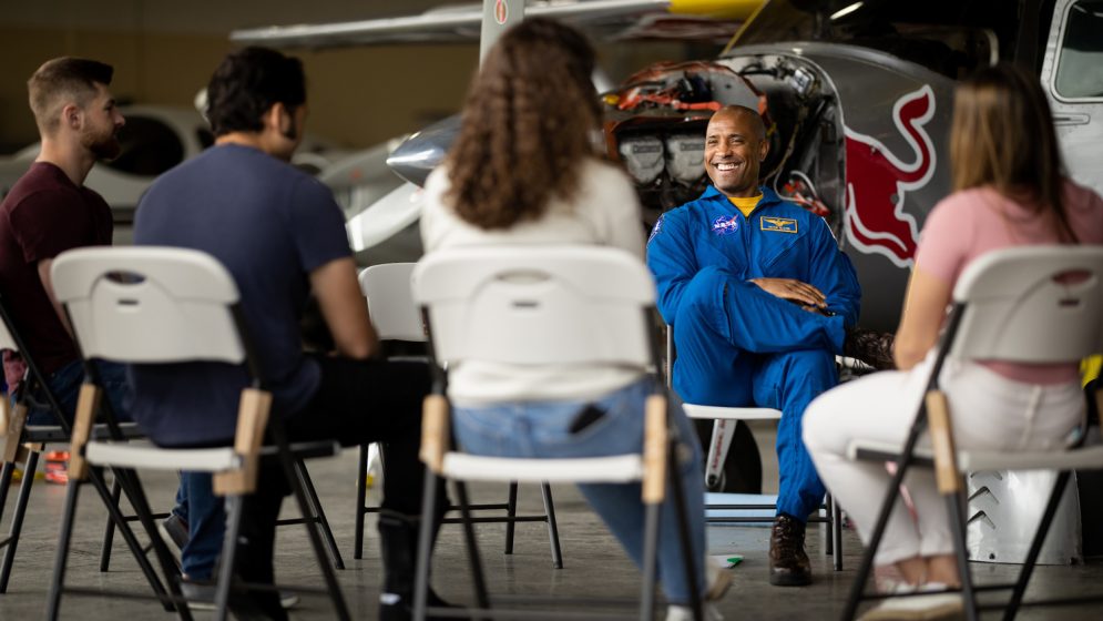 Astronaut Victor Glover smiles while talking to students near an airplane in a hangar
