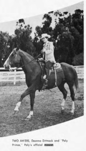 A young woman in western gear rides a horse in a black and white photo