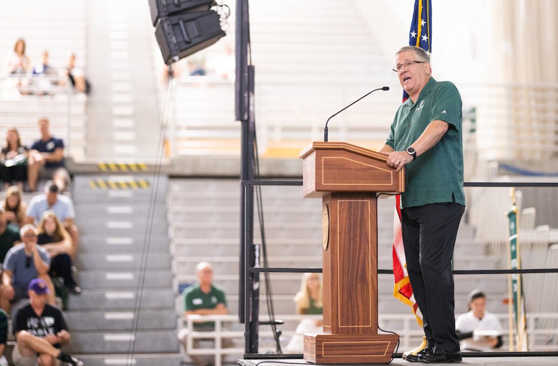 President Armstrong in a green shirt speaking from a podium