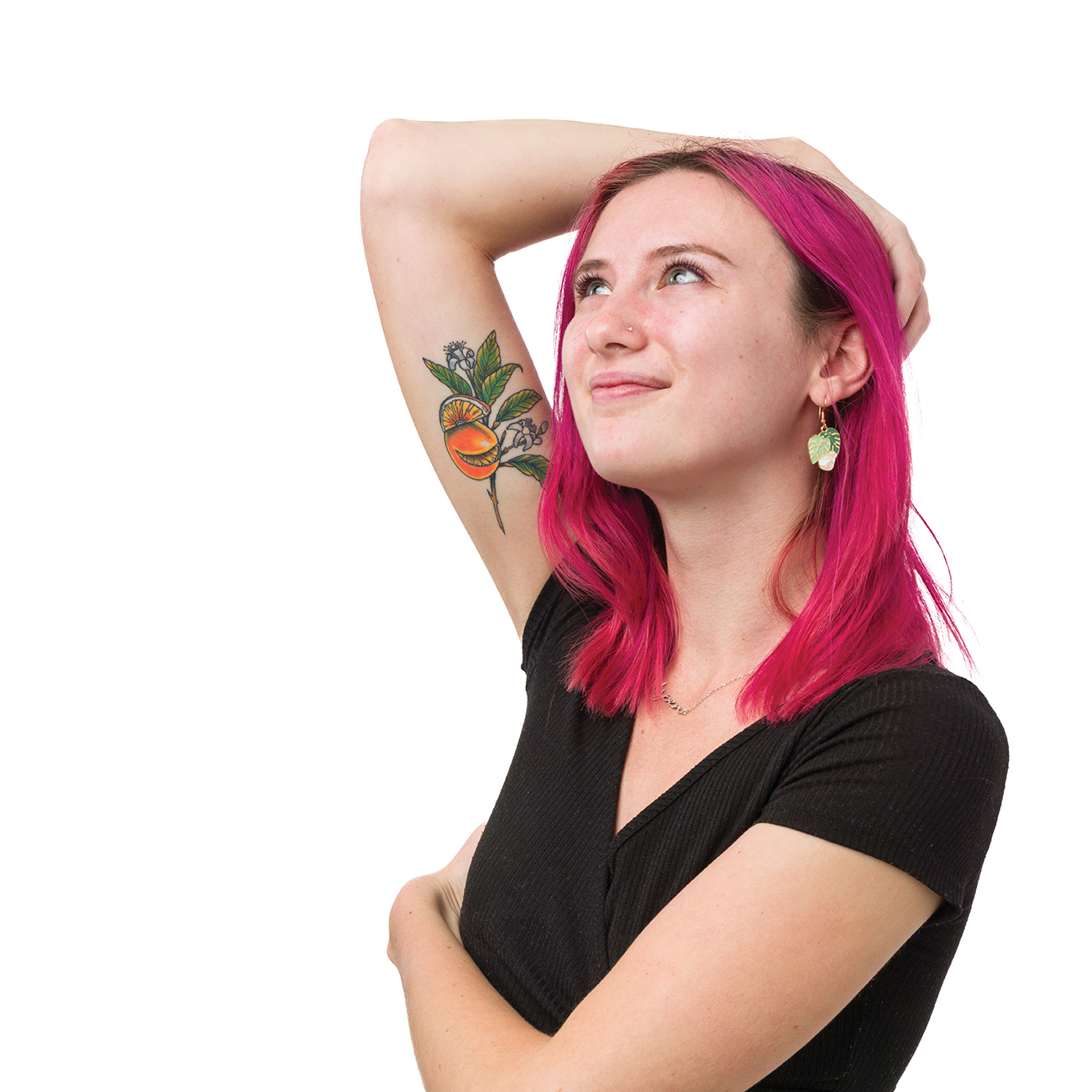 A young woman with pink hair raises her arm to display a brightly colored tattoo of oranges, a branch and orange blossoms