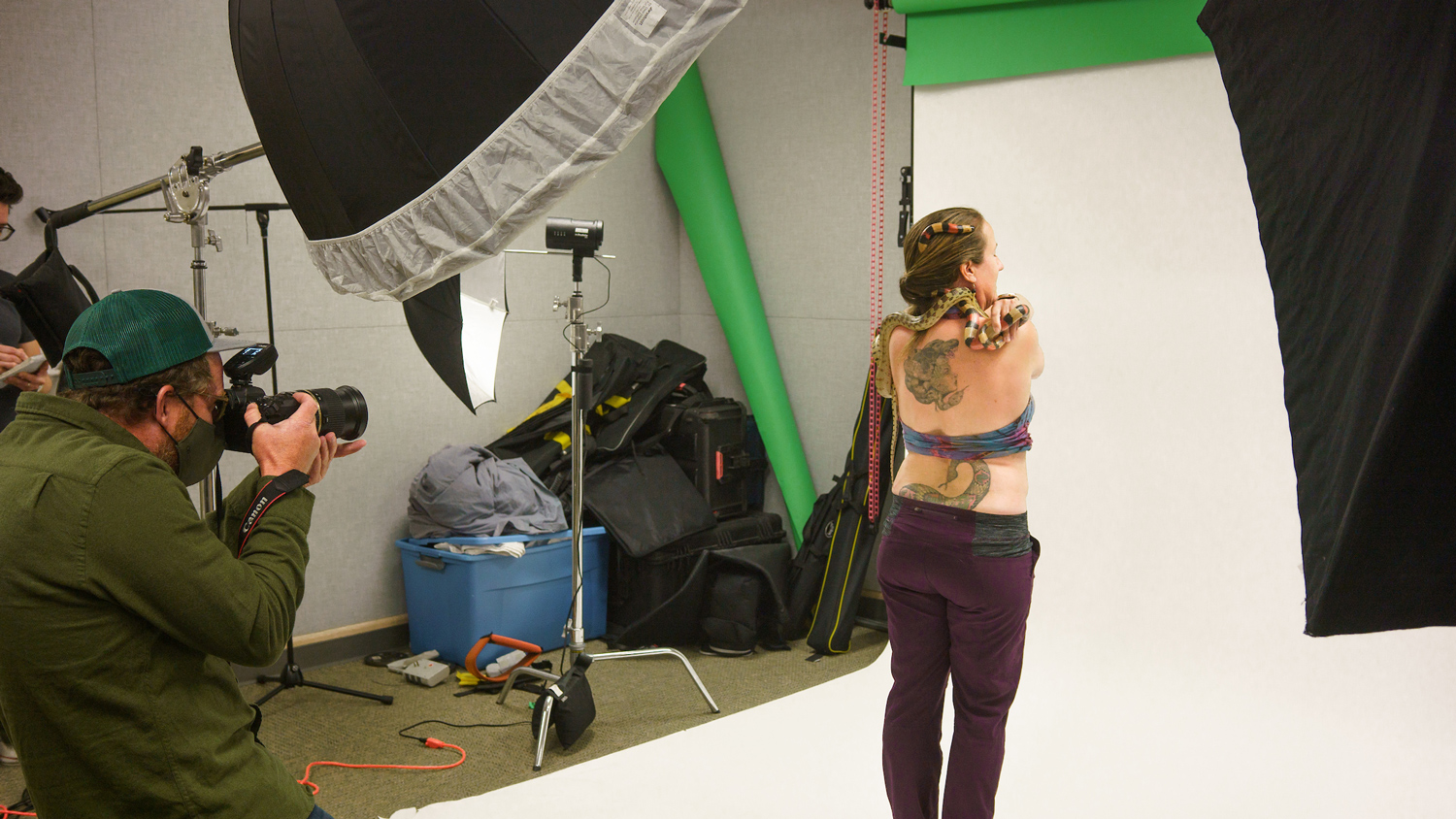 A photographer takes photos of a person holding snakes in a studio with lights and a white backdrop