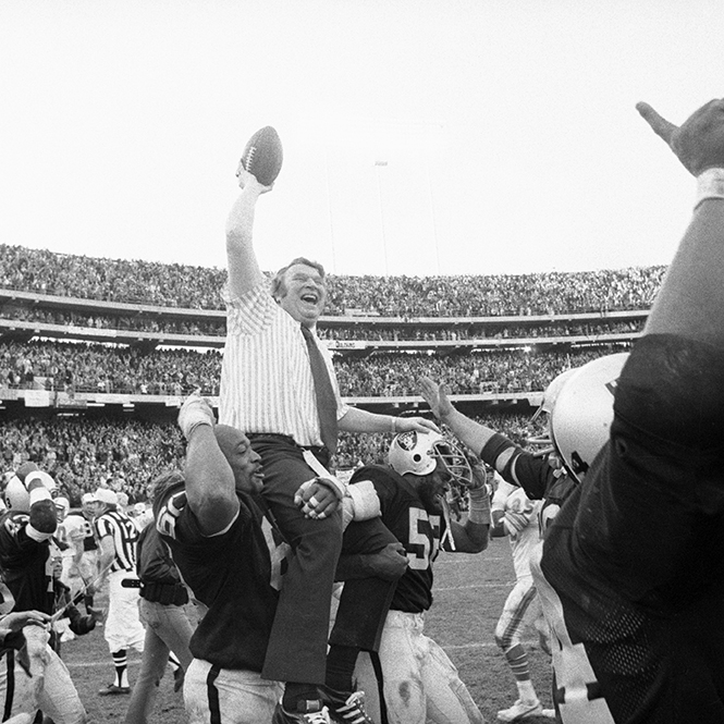 Two Raiders players carry Madden onto the field in a packed football stadium