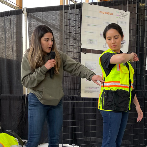 Lizette Galvez holds a microphone while inspecting a modified safety vest on a student