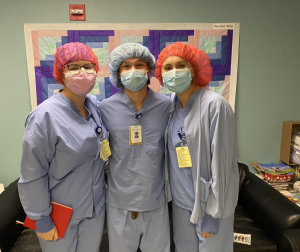 Three students pose for a photo in hospital scrubs, caps and surgical masks