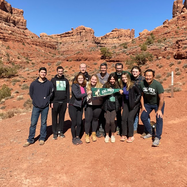 A group of Cal Poly students and faculty hold a green pennant in the desert