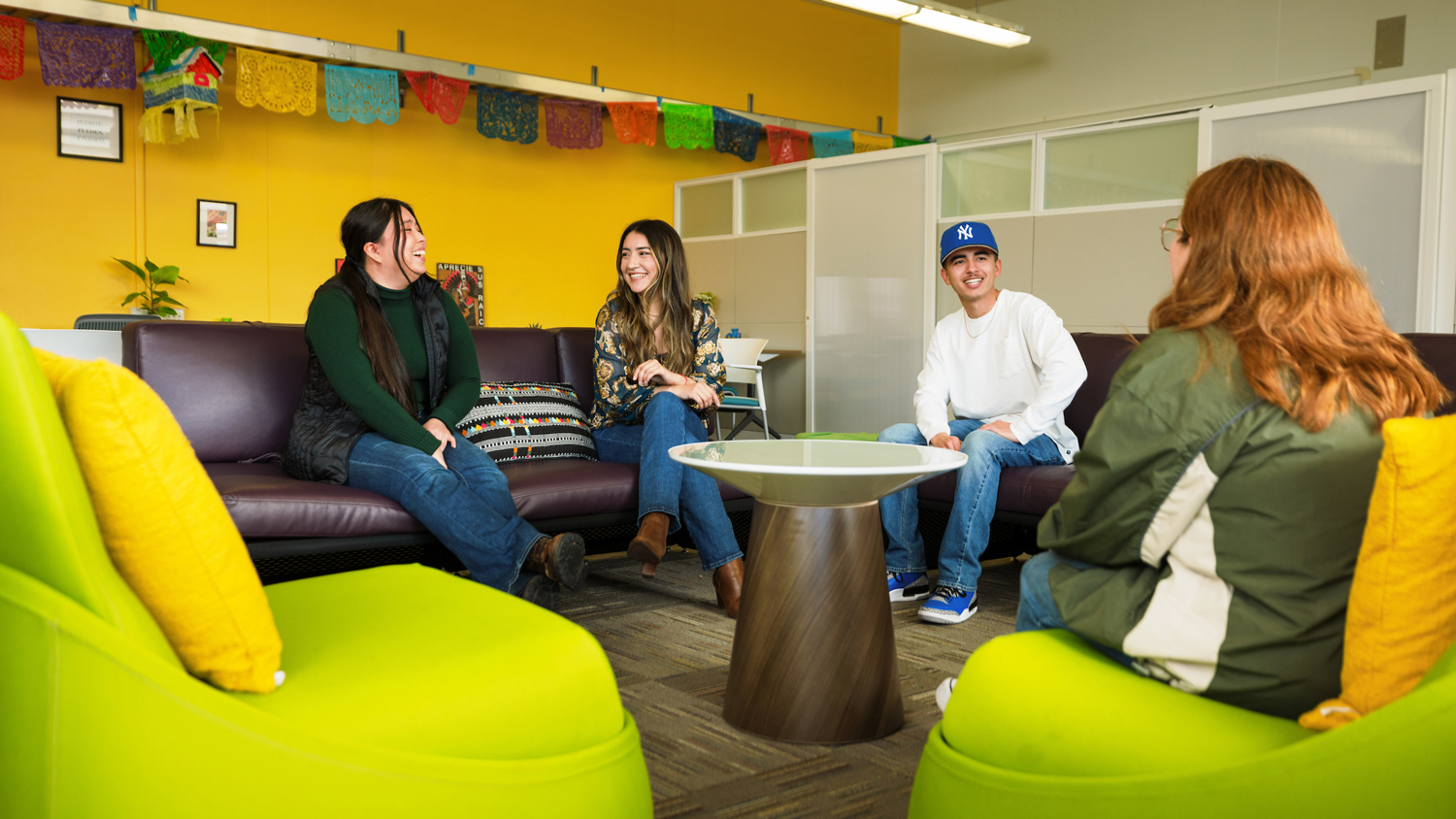 Four people sit on couches in a student center with yellow walls and colorful decorations