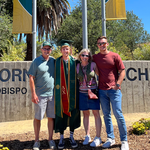 Four people smile in front of Cal Poly's campus entrance banners