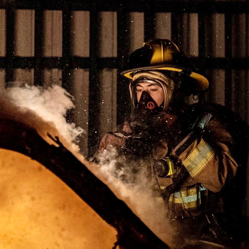 Michael Kusaba in firefighter's gear near a burning car