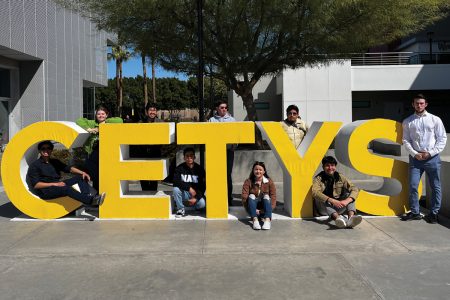 Nine students pose near large yellow letters that spell out CETYS in Mexicali ahead of a Spanish language debate