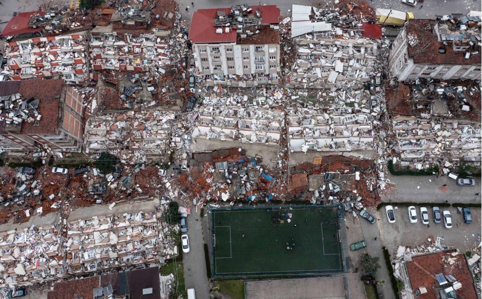 An aerial photo of an entire neighborhood of collapsed buildings — one still standing in the center.