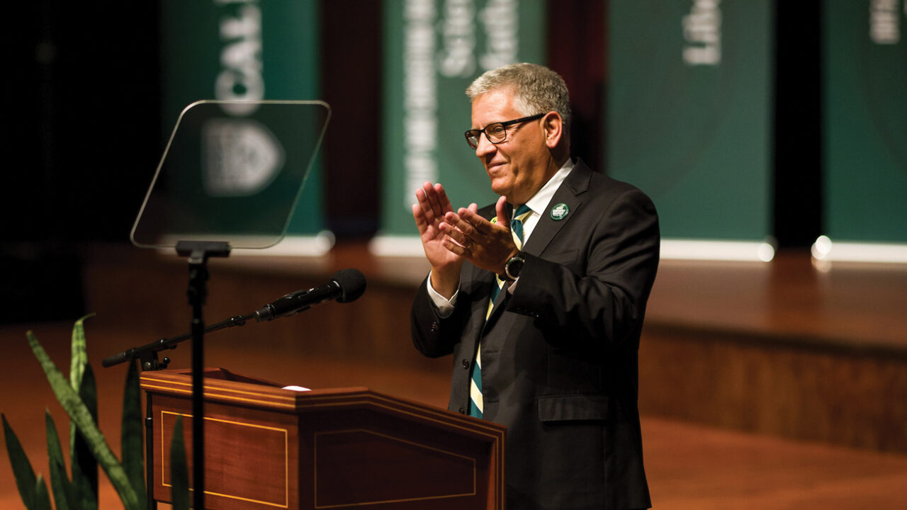 President Armstrong claps at a podium at Fall Convocation
