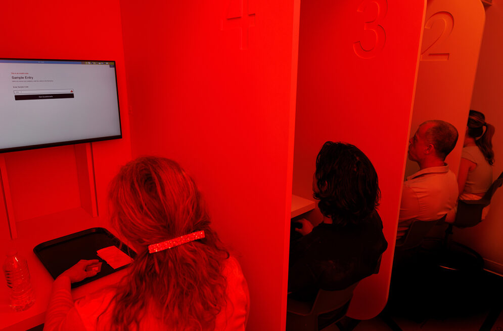 People sit in tasting booths in a room flooded with red light.