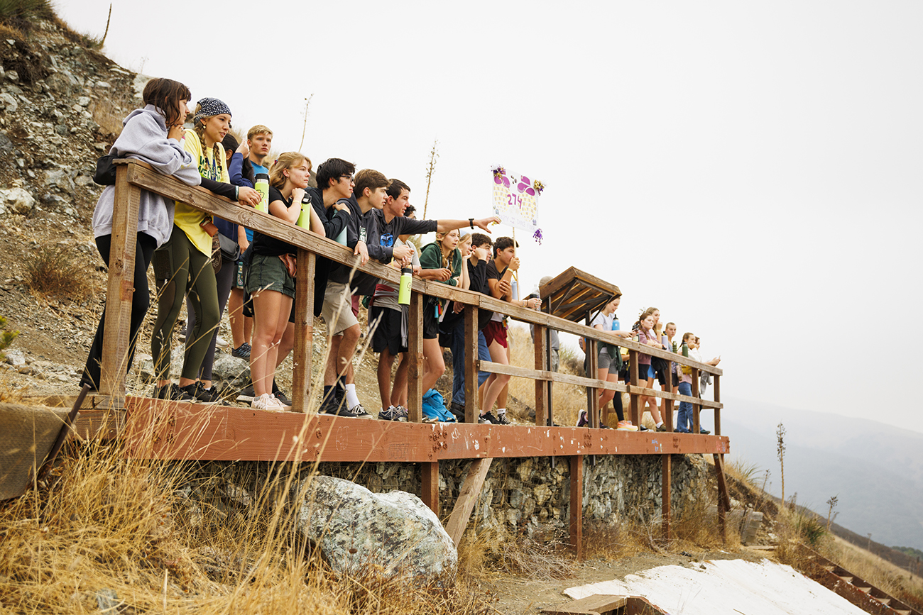 A group of students lines up to look out over the railing on a hillside platform above the Cal Poly P.