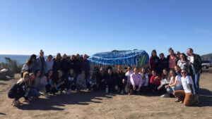 The members of Cal Poly's Surfrider Club pose for a photo at the beach, holding up a banner promoting beach cleanup