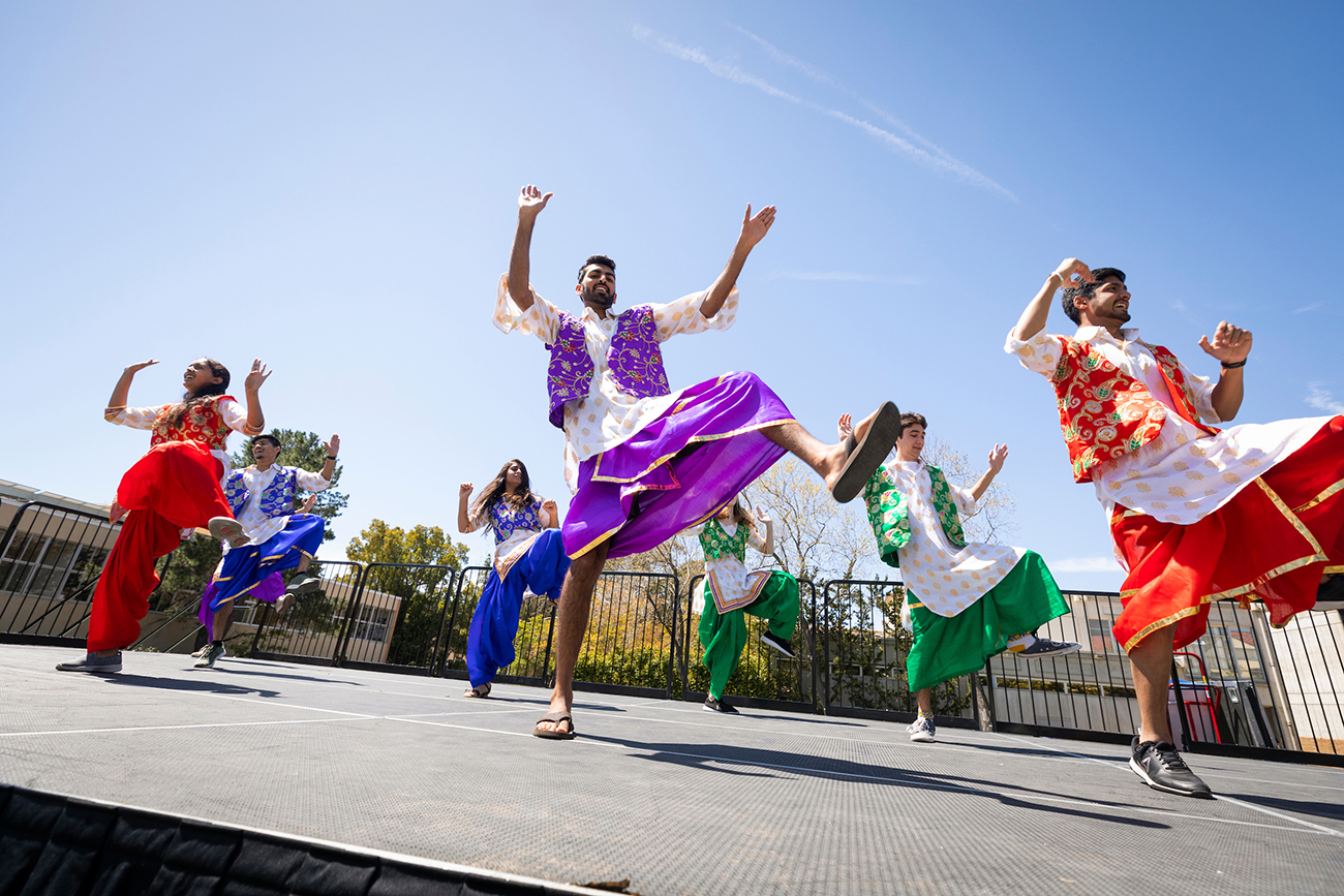A group of students in traditional Indian costumes perform a dance on an outdoor stage.