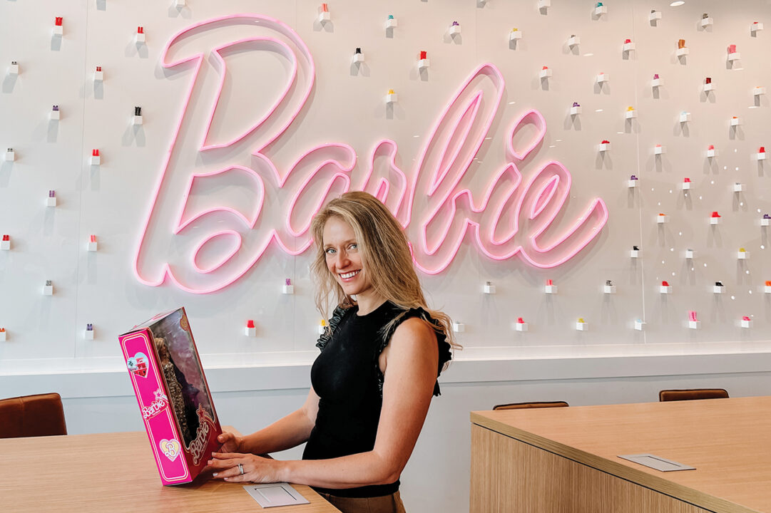 Alumna Krista Berger, holding a pink Barbie box in front of a colorful wall with Barbie written on it in pink