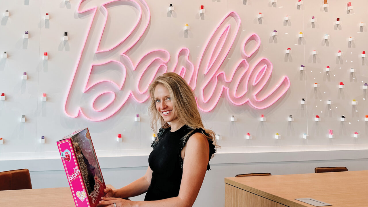 Krista Berger holding a Barbie doll box near a pink neon Barbie sign