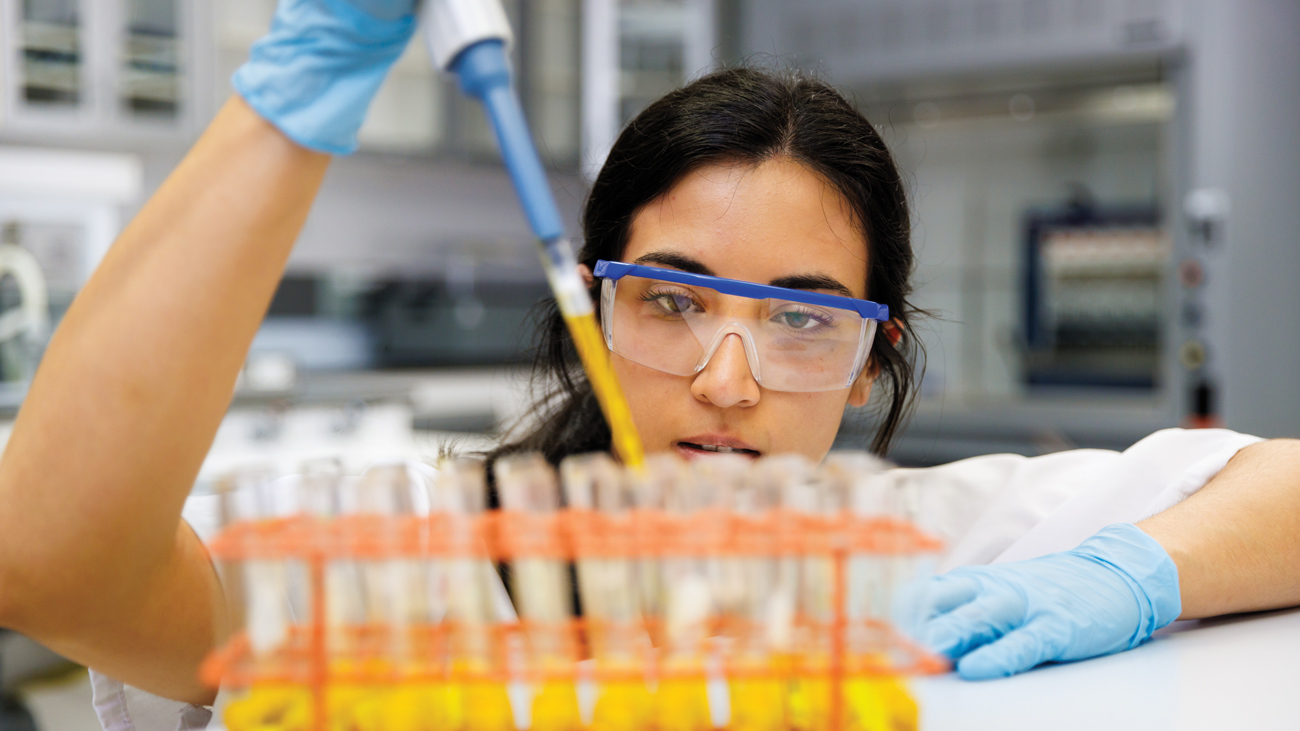 A student researcher wearing protective glasses and gloves fills a vial.