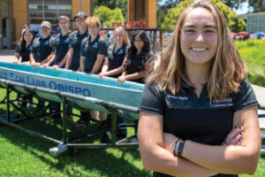 Eight students in black polo shirts stand next to a concrete canoe that reads Cal Poly San Luis Obispo
