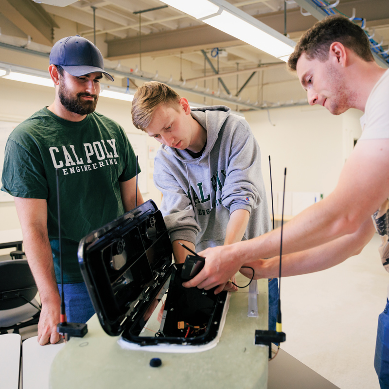 Three students work on an autonomous boat's engine in an engineering lab