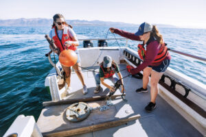 Three Cal Poly students deploy audio data analysis tools from a boat off the coast of California