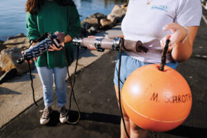 Two Cal Poly students hold underwater audio recording devices on a dock.