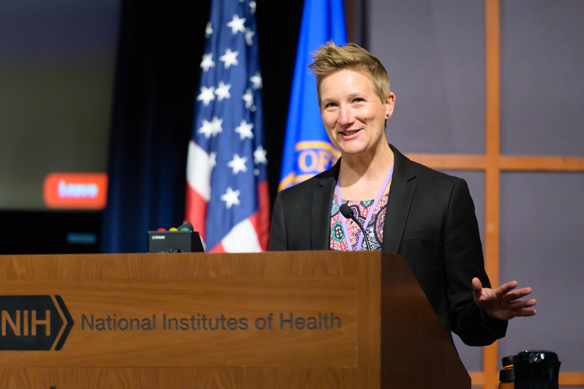A person speaks behind a wooden podium with the National Institutes of Health logo near an American flag