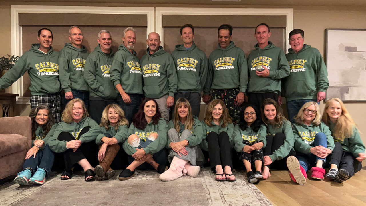 A group of 18 people smile wearing green sweatshirts that say Cal Poly Thanksgiving