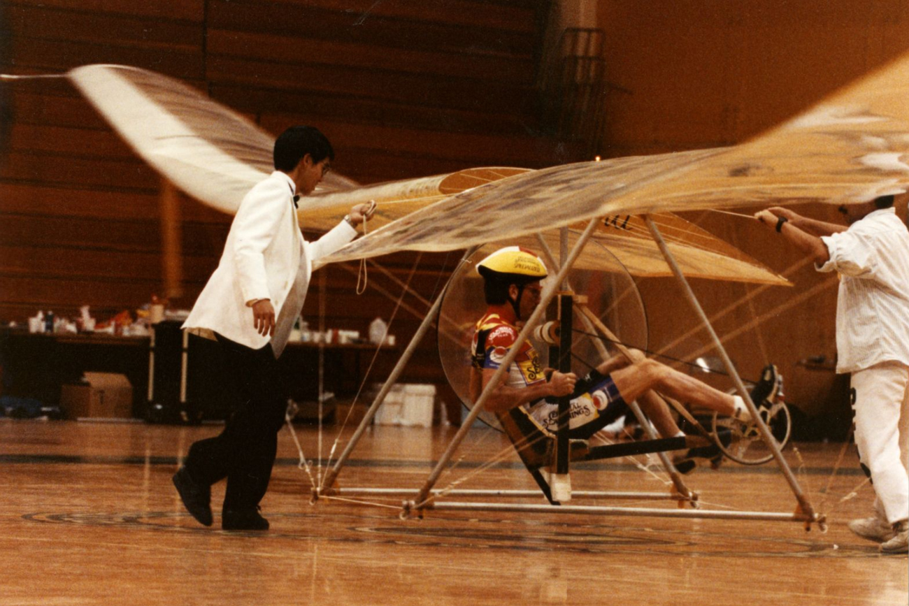 Three people tend to a human-powered helicopter in a gymnasium