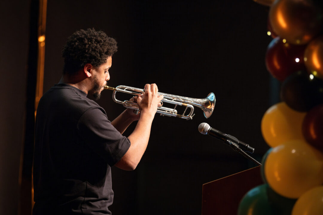 A student plays a trumpet in front of a microphone and colorful balloons.