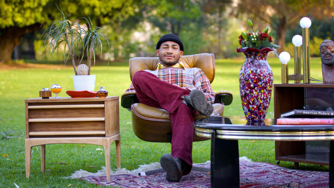 Adam Kemp sits on vintage furniture on a green lawn