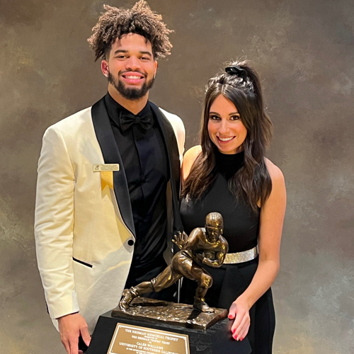 Katie Ryan stands with the Heisman Trophy and football player Caleb Williams