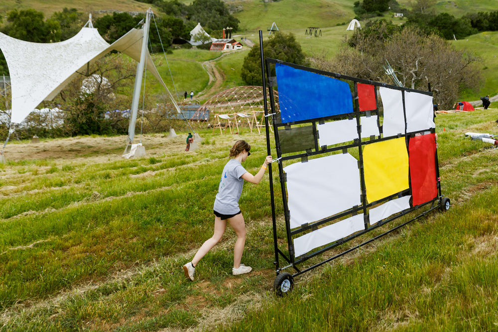 A student pushes a colorful structure wall mounted on wheels through Poly Canyon's hillside