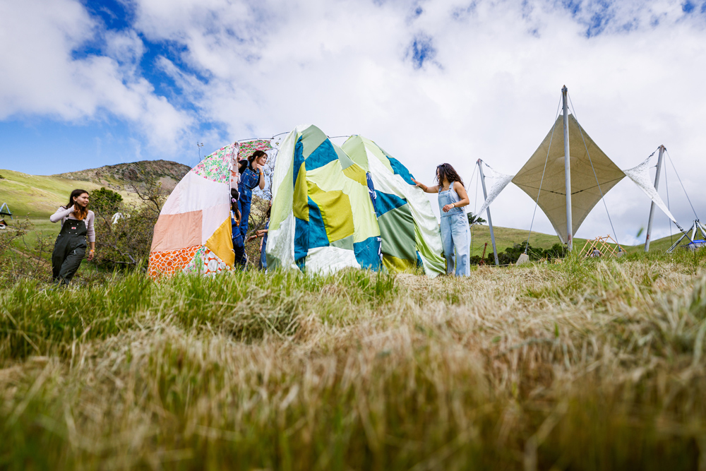 Students assemble a structure made of colorful fabric and a metal frame on a hillside near Poly Canyon structures